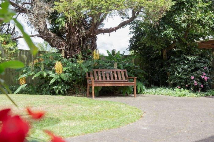 Wooden bench in garden with flowers and trees.